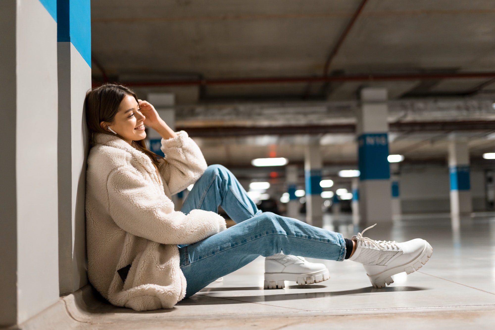 Fashionable girl sits on the floor of underground parking with wireless headphones